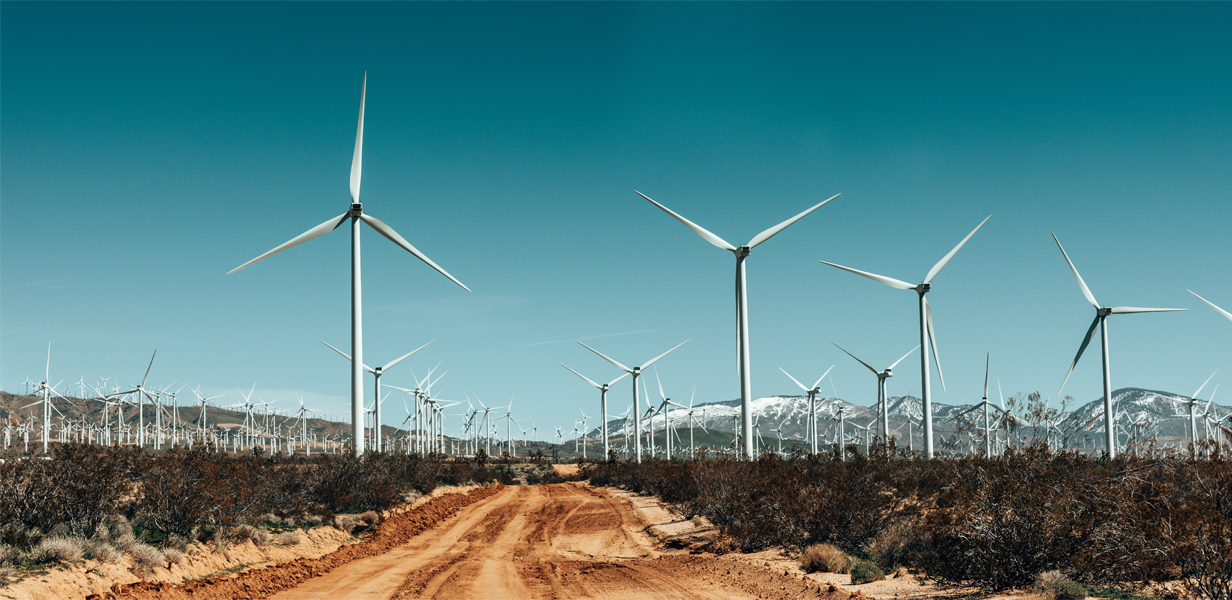 Wind mills, dirt road, mountains in the background with snow