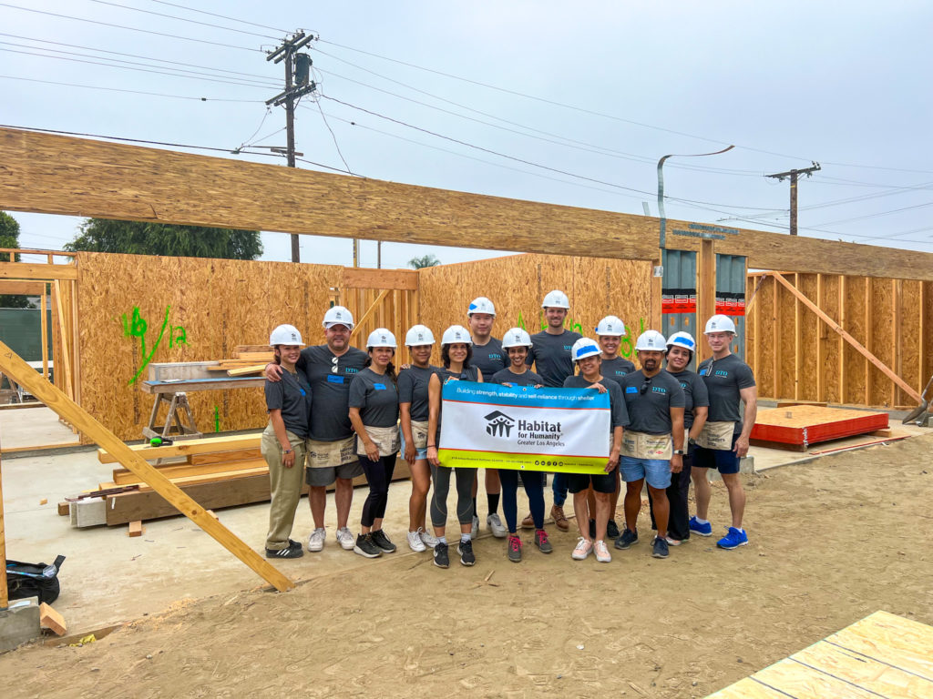 Group of DTO employees at the Habitat for Humanity construction site, holding a banner.